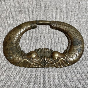 Könnte beinhalten: Ein Türklopfer aus Messing in Form von zwei Fischen, deren Schwänze ineinander verschlungen sind. Die Fische haben detaillierte Schuppen und Flossen.