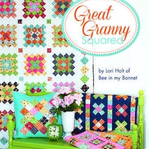 May include: A colorful quilt with a patchwork design, a pillow, and a blanket are displayed on a green bench. The book "Great Granny Squared" by Lori Holt of Bee in my Bonnet is visible. The quilt and pillow feature squares of various colors.