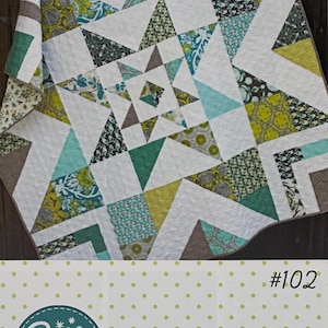 May include: A quilt with a starburst design, featuring white, teal, green, and brown geometric shapes. The quilt has the text "TRIPLE BARNSTAR" and the Amy Gibson logo. The pattern is #102 and is fat quarter and layer cake friendly.