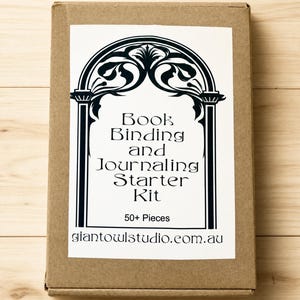 May include: A rectangular brown cardboard box featuring a white label with a black decorative arch design. The text reads Book Binding and Journaling Starter Kit, 50+ Pieces, and giantowlstudio.com.au in a stylised black font on the white label.