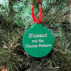 May include: Green Christmas bauble with the text "Blessed are the Cheese Makers" in white lettering.