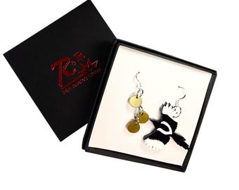 May include: A pair of earrings featuring a black and white bird design with gold-colored disc accents. The earrings are displayed in a black box with a red logo. The earrings are on a white background.