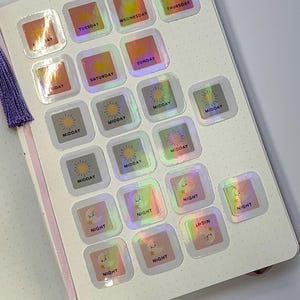 May include: A collection of square holographic stickers arranged on a dotted journal page. The stickers feature sun icons labeled Tuesday, Wednesday, Thursday, Friday, Saturday, Sunday, Midday, and moon icons labeled Night in dark text.