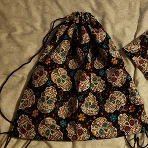 Puede incluir: Una bolsa de cord&oacute;n negro con un patr&oacute;n de calavera de az&uacute;car colorido. La bolsa tiene un cord&oacute;n negro y est&aacute; hecha de una tela suave.