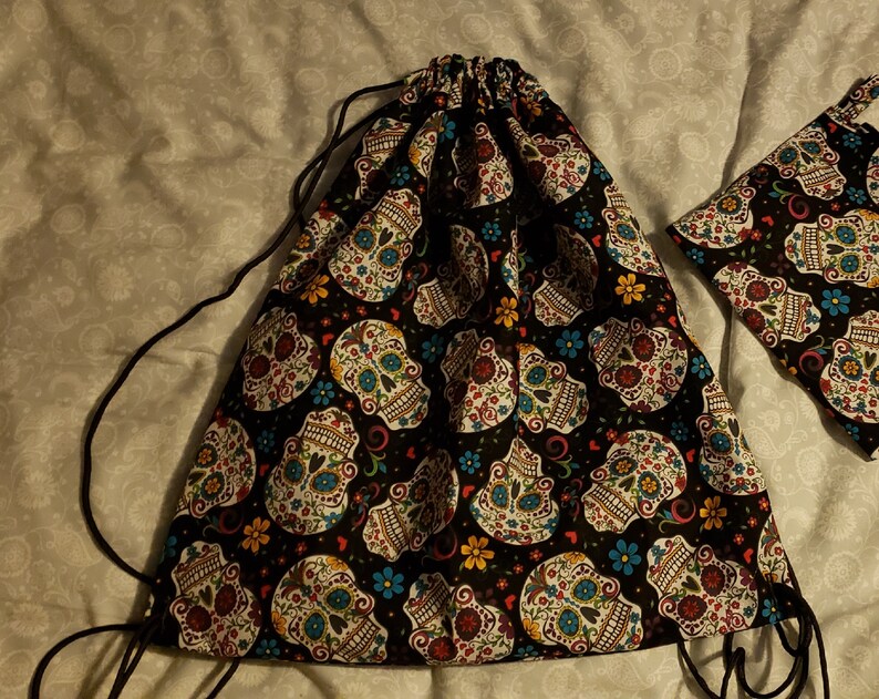 Puede incluir: Una bolsa de cord&oacute;n negro con un patr&oacute;n de calavera de az&uacute;car colorido. La bolsa tiene un cord&oacute;n negro y est&aacute; hecha de una tela suave.