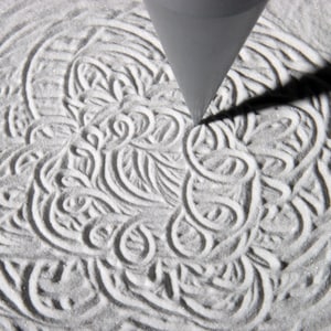 May include: A close-up of a cone-shaped tool creating intricate patterns in a bed of white sand.