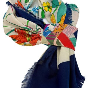 May include: A colorful scarf with a floral pattern and a navy blue border. The scarf features a patchwork design in the center, with a variety of colors and patterns. The scarf has fringed edges.