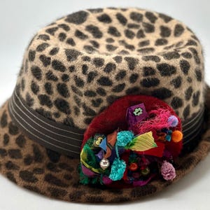 May include: A brown and black leopard print fedora hat with a wide brim and a colorful fabric flower embellishment.