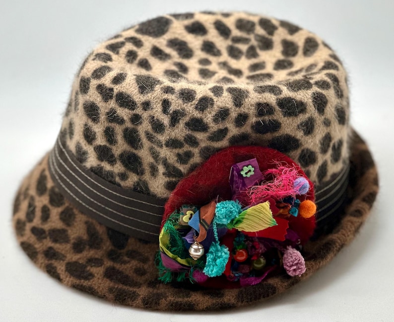 May include: A brown and black leopard print fedora hat with a wide brim and a colorful fabric flower embellishment.