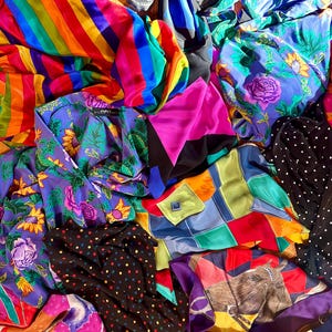 May include: A colorful assortment of fabric scraps in various patterns, including stripes, polka dots, and floral designs. The fabrics are in shades of blue, green, pink, yellow, and orange.