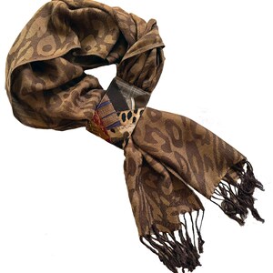 May include: A brown scarf with a leopard print pattern and dark brown fringe. The scarf is knotted with a decorative patch featuring various fabric patterns and colors, including blue, black, and tan.