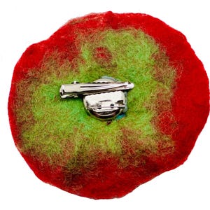 May include: Back view of a felt flower brooch with a red and green color scheme. The brooch has a silver pin and clasp.