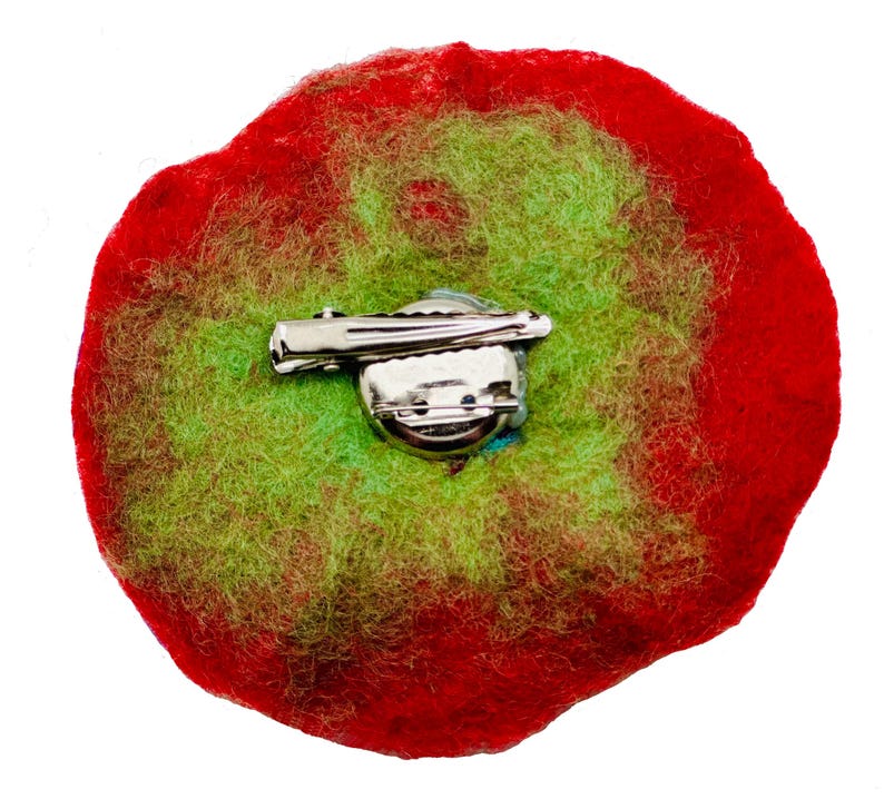 May include: Back view of a felt flower brooch with a red and green color scheme. The brooch has a silver pin and clasp.