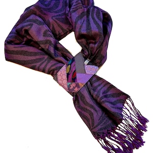 May include: A purple scarf with a zebra stripe pattern and a decorative patch. The scarf has a fringed edge and is made of a soft, flowing fabric. The patch is made of various patterned fabrics in shades of purple, pink, and blue.