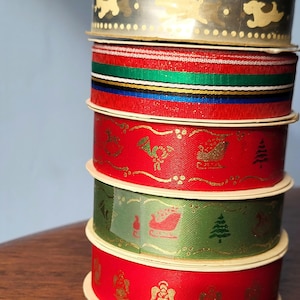 Peut inclure: Un rouleau de ruban de Noël rouge, vert et or avec des motifs de traîneau, d'arbre et d'étoile.