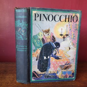 May include: A vintage hardback book titled "Pinocchio" by C. Collodi, illustrated by Maud and Miska Petersham. The cover features a colourful illustration of Pinocchio sleeping in bed, surrounded by a cricket, an owl, and a bird.