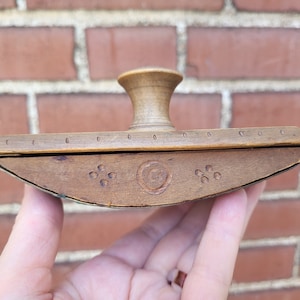 Może przedstawiać: Drewniany kałamarz z rzeźbionym wzorem. Kałamarz ma okrągły wierzch i płaskie dno. Kałamarz jest wykonany z jasnobrązowego drewna i ma ciemnobrązowe zabarwienie.