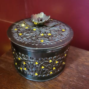 Peut inclure: Une boîte décorative en métal noir avec un motif floral et des accents jaunes. Le couvercle a un bouton en forme de fleur.