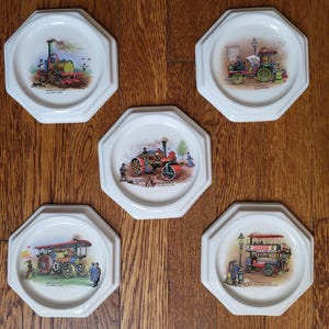 May include: Set of five white octagonal coasters. Each coaster features a colorful illustration of vintage steam-powered vehicles, including tractors and buses. The coasters are arranged on a wooden surface.