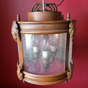Könnte beinhalten: Ein Holzrahmen-Kronleuchter mit einem mattierten Glasschirm und einem dekorativen Blattdesign. Der Kronleuchter hat drei Glühbirnen.