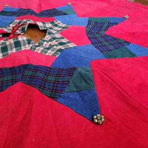 May include: Red, blue and green plaid patchwork Christmas tree skirt with a star design and silver bells.