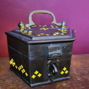 May include: A dark brown wooden box with a brass handle and gold accents. The box has a hinged lid and a lock with a keyhole. The box is decorated with small gold squares and stars.