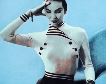 May include: A white sweater with black and white stripes on the collar and cuffs. The sweater has a button detail on the front.