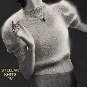 May include: A pale grey knitted jumper with short, puffed sleeves. The jumper has a crew neck and a ribbed hem. A pendant necklace with a dark stone hangs on the chest. The text "STELLAR KNITS 4U" is in the lower left corner.