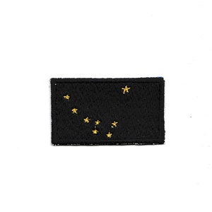 以下が含まれることがあります： アラスカ州の州旗、北斗七星（おおぐま座）を表す8つの金色の星が刺繍された黒い布のパッチです。