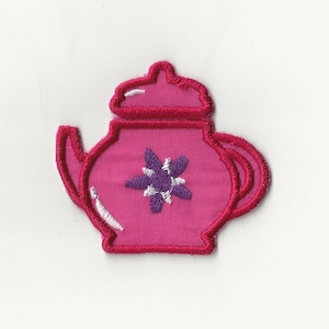 May include: A pink embroidered teapot with a purple flower design.