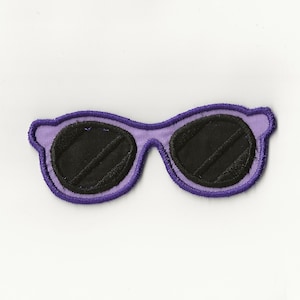 May include: Purple sunglasses with black lenses. The sunglasses are a fabric patch.