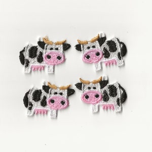 May include: Four black and white cow appliques with pink noses and brown ears. The cows are embroidered and have a white background.
