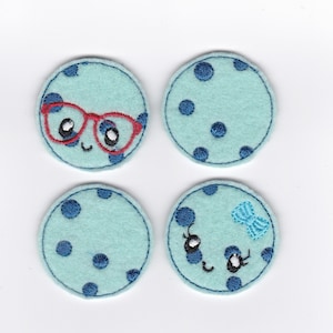 Puede incluir: Cuatro círculos de fieltro azul con lunares blancos. Un círculo tiene un par de gafas rojas y una cara sonriente. Otro círculo tiene un lazo azul y una cara con pestañas. Los otros dos círculos son lisos.