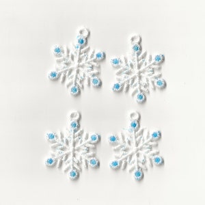 Puede incluir: Cuatro adornos de copo de nieve blancos con detalles azules. Los copos de nieve están bordados y tienen un lazo en la parte superior para colgar.