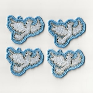 Op de afbeelding: Vier witte duiven geborduurde patches op een lichtblauwe achtergrond. De duiven vliegen met hun vleugels uitgespreid.