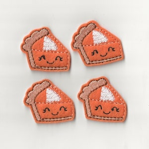 Puede incluir: Cuatro rebanadas de pastel de calabaza de fieltro con caras sonrientes y glaseado blanco. Las rebanadas de pastel son de color naranja y tienen una corteza marrón.