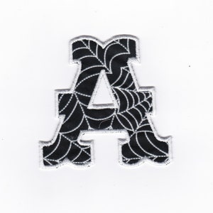 May include: A black felt letter A with a white spiderweb pattern. The letter is outlined in white.