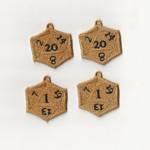 Könnte beinhalten: Vier braune, gestickte, sechseckige Würfel mit schwarzen Zahlen. Die Würfel sind 20-seitig, 12-seitig, 10-seitig und 6-seitig.