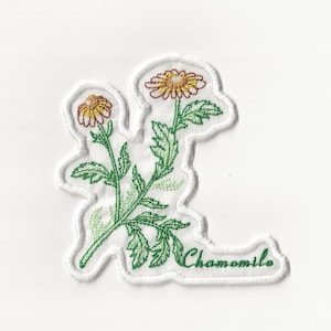 Op de afbeelding: Witte geborduurde patch met een groene stengel en bladeren, twee gele en oranje bloemen en het woord "Chamomille" in groene cursieve letters.