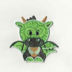 Könnte beinhalten: Grüne und schwarze gestickte Applikation eines Cartoon-Drachen mit einem Wirbelmuster. Der Drache hat große Augen und einen kleinen Mund.