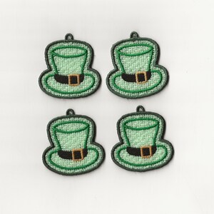 Peut inclure: Quatre patchs en tissu vert feutré avec une image brodée d'un chapeau de lutin avec une boucle dorée. Les chapeaux sont soulignés de fil noir.