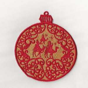 May include: Red and gold Christmas bauble with an embroidered design of the three wise men riding camels. The bauble is shaped like a circle with a small loop at the top.