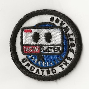 May include: A white embroidered patch with a black border. The patch features a blue and white cassette tape with the words "Low Laser" and a red rectangle with a white line. The text around the cassette tape reads "Buy Music, Support the Artists, Updated the System".