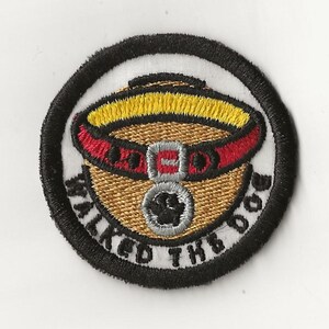 May include: A round, black and white embroidered patch with the text "Walked the Dog" and a cartoon image of a dog wearing a red collar with a silver tag.