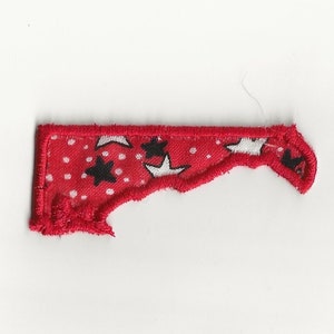 May include: A red fabric patch with white and black stars. The patch is shaped like a state outline and has a frayed edge.