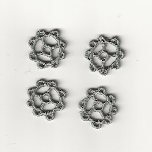 Könnte beinhalten: Vier silberfarbene, zarte, gehäkelte Spitzendeckchen mit kreisförmigem Design.