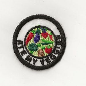 May include: A black and white embroidered patch with a white circle in the center. The circle contains a variety of colorful vegetables and the text "ATE MY VEGGIES".