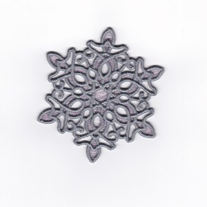 Puede incluir: Un diseño de bordado en forma de copo de nieve plateado con un patrón delicado e intrincado.