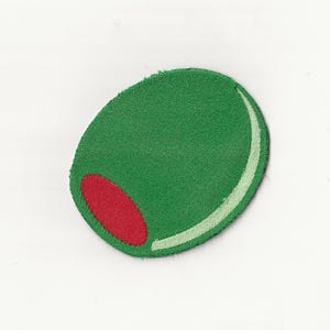 以下が含まれることがあります： 赤い種と白いアクセントが付いた、緑色のオリーブ型のパッチ。パッチは布製で、テクスチャ加工された表面を持っています。デザインはシンプルで大胆で、衣類やアクセサリーにちょっとした楽しさを加えるのに最適です。