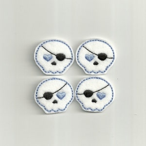 May include: Four white felt skull patches with blue hearts for eyes and black eyepatches. The skulls are outlined in blue thread.